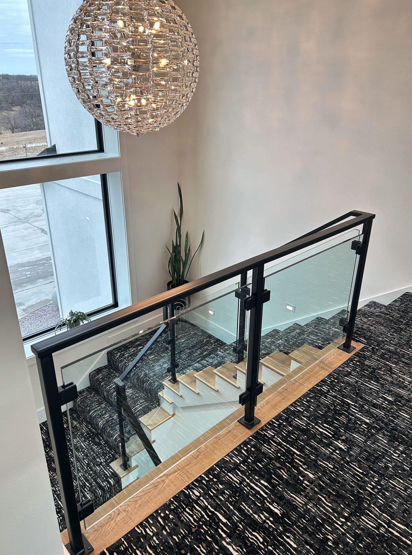 Patterned carpet stair runner below a crystal chandelier and glass railing in a tall stairwell