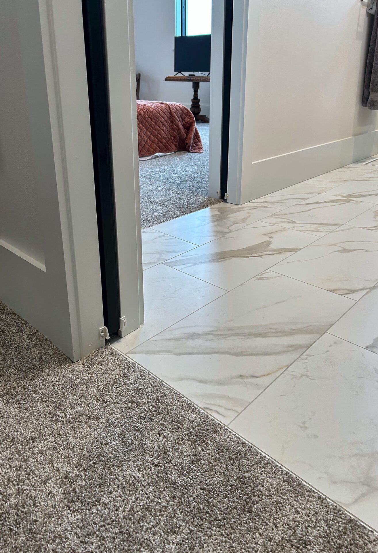 Clean transition where marble-look porcelain tile meets plush carpet at a bedroom doorway